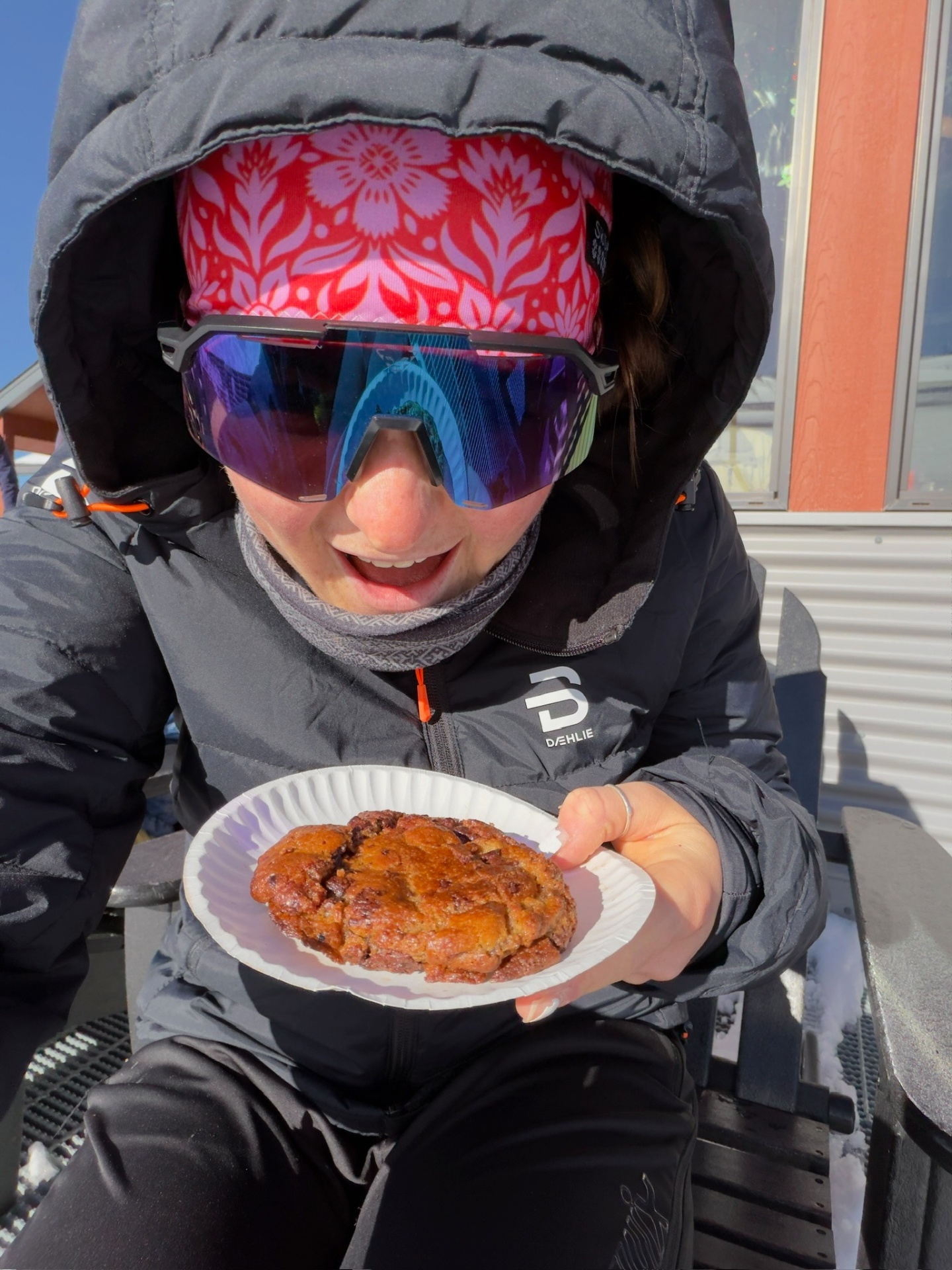 Bayli in a Bjørn Dæhlie puffer and 100% shades holding a cinnamon roll after a nordic session