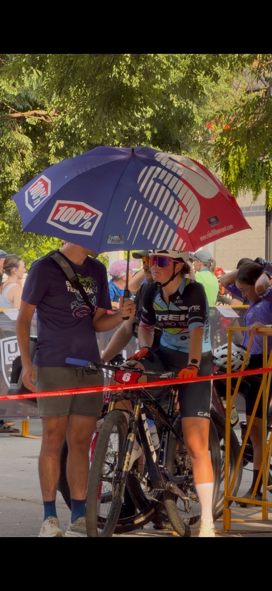 Bayli under a 100% umbrella at a UCI staging area, bib #6
