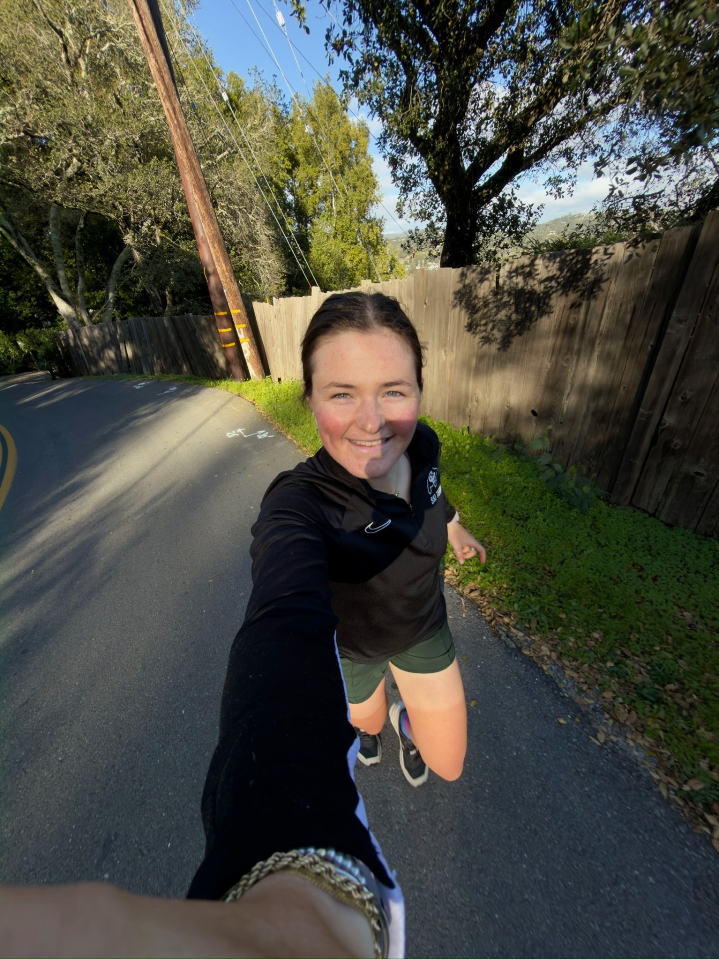 Bayli running in a CU Ski Team quarter-zip on a Bay Area road, selfie