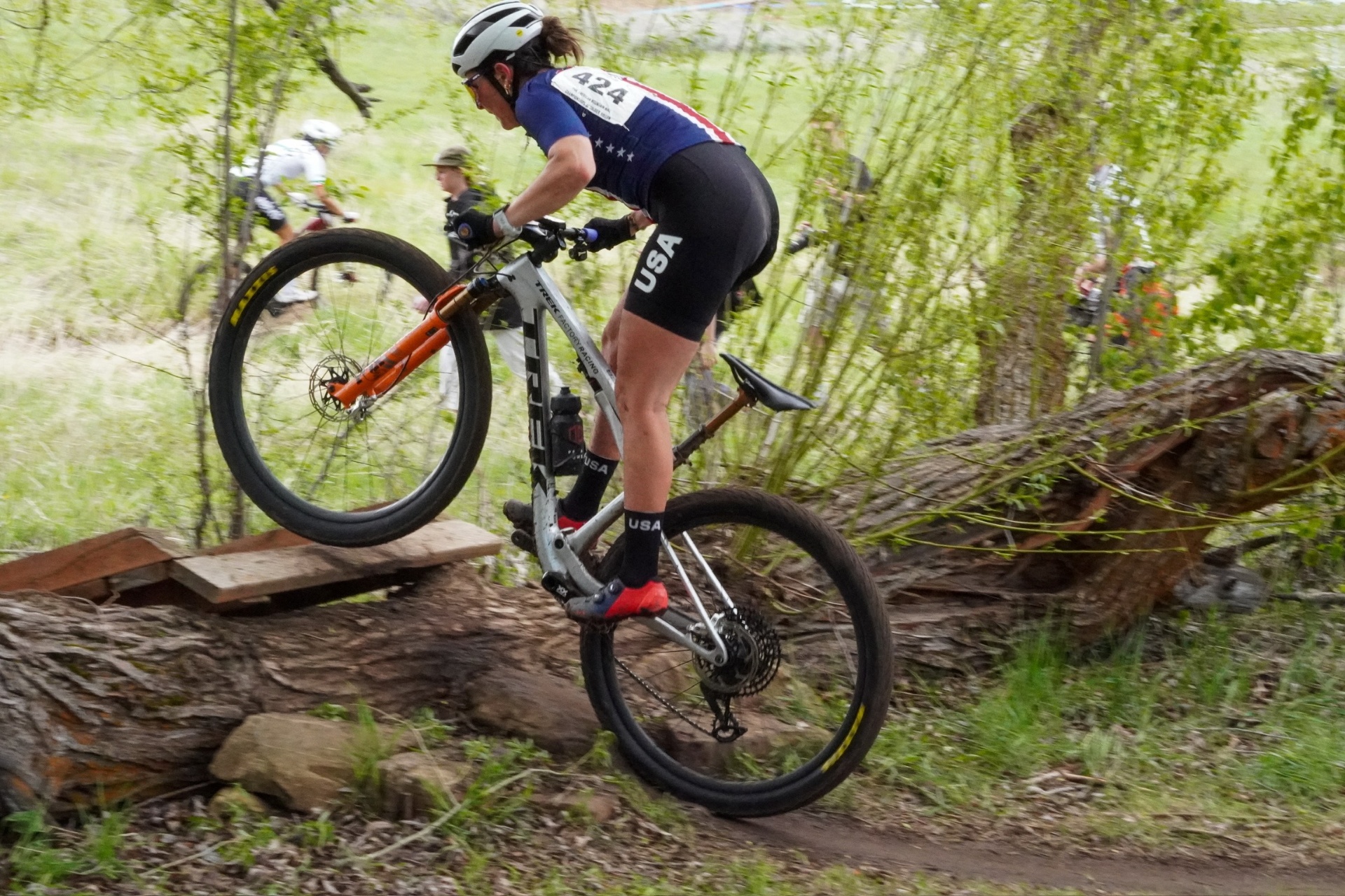 Bayli in USA National Team kit manualing over a log feature at US Pro XCT