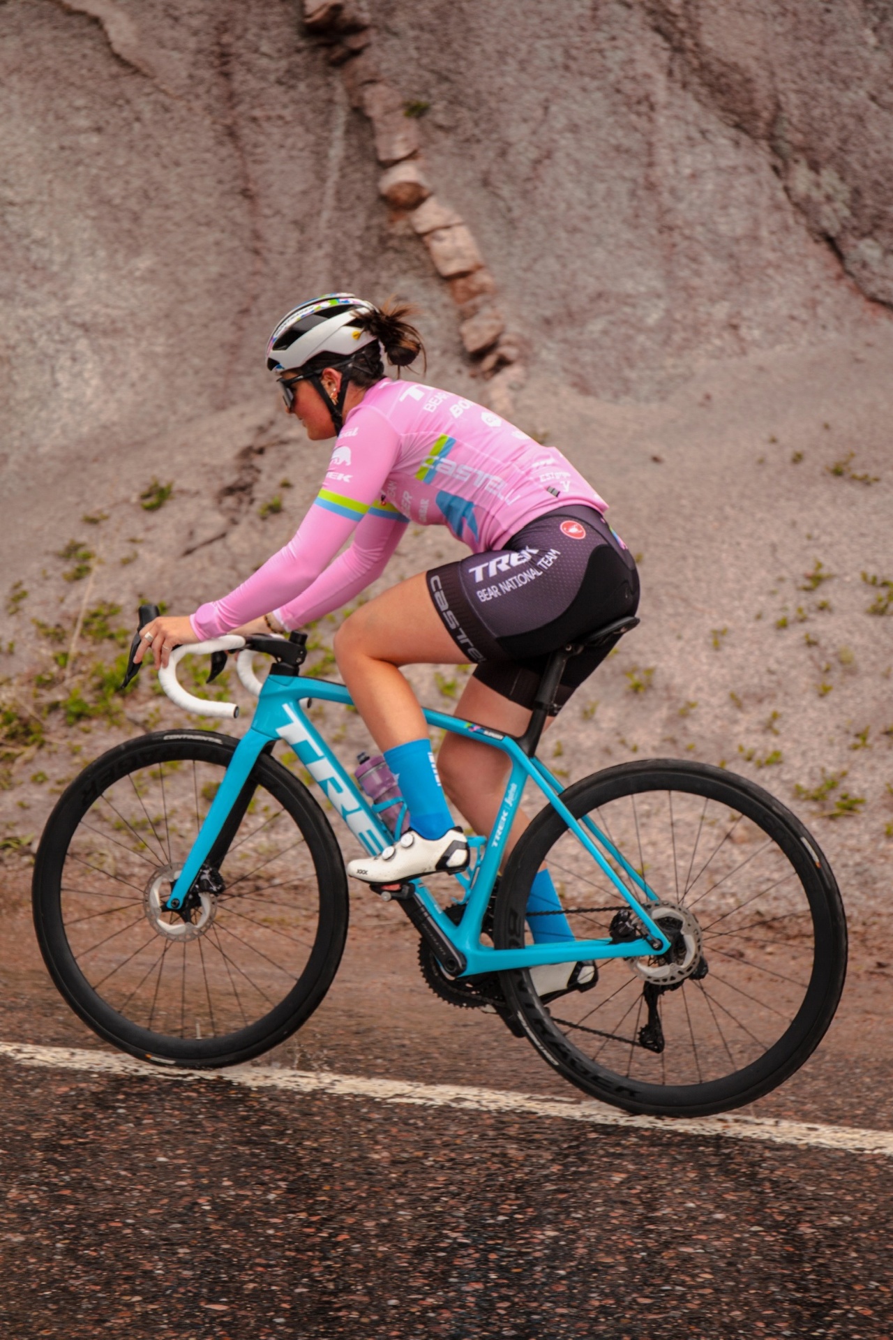 Bayli riding a Trek road bike past a granite wall in a pink Castelli long-sleeve kit
