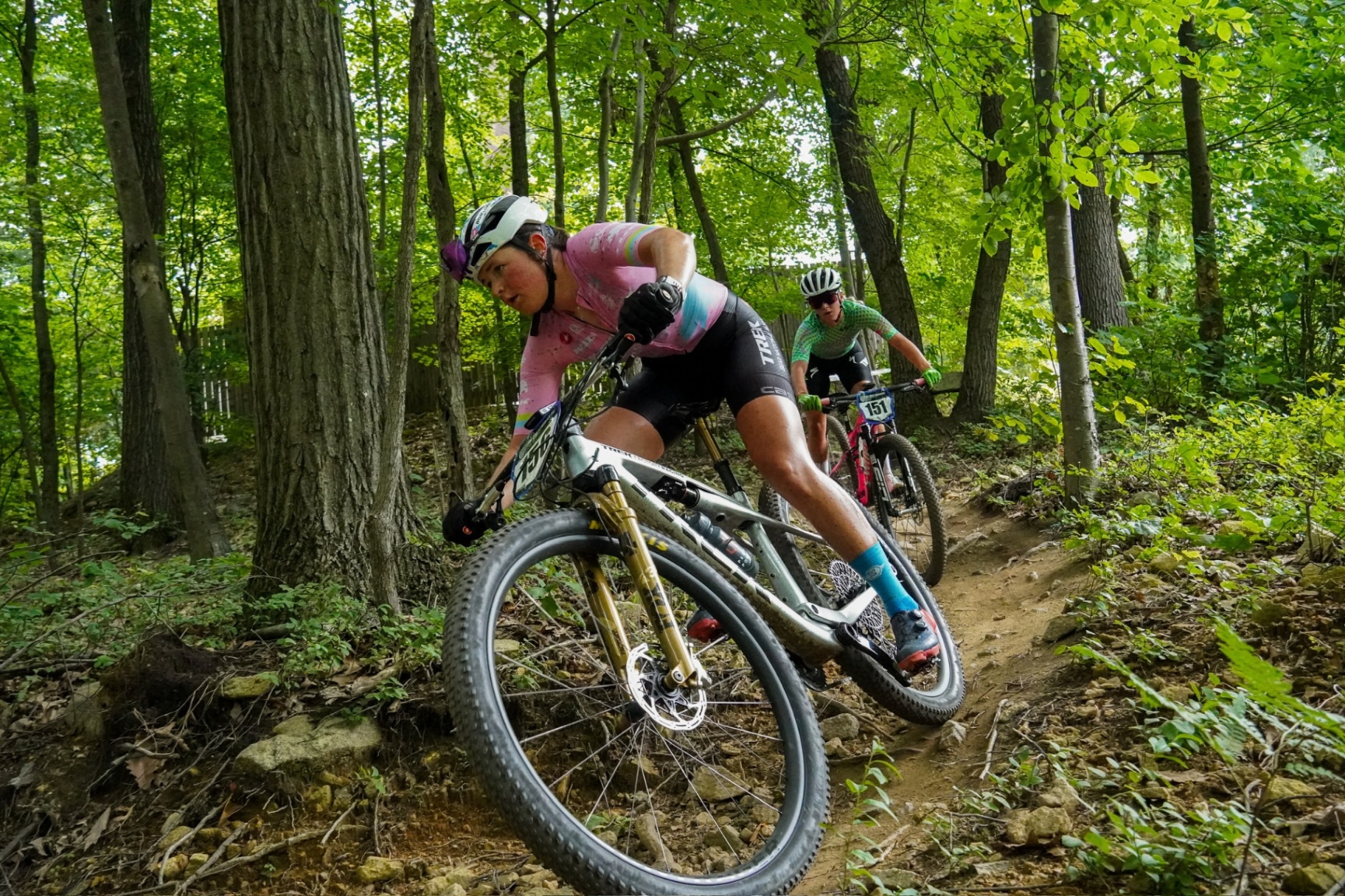 Bayli railing a rooty singletrack corner in a pink Bear Pro kit through Midwest woods