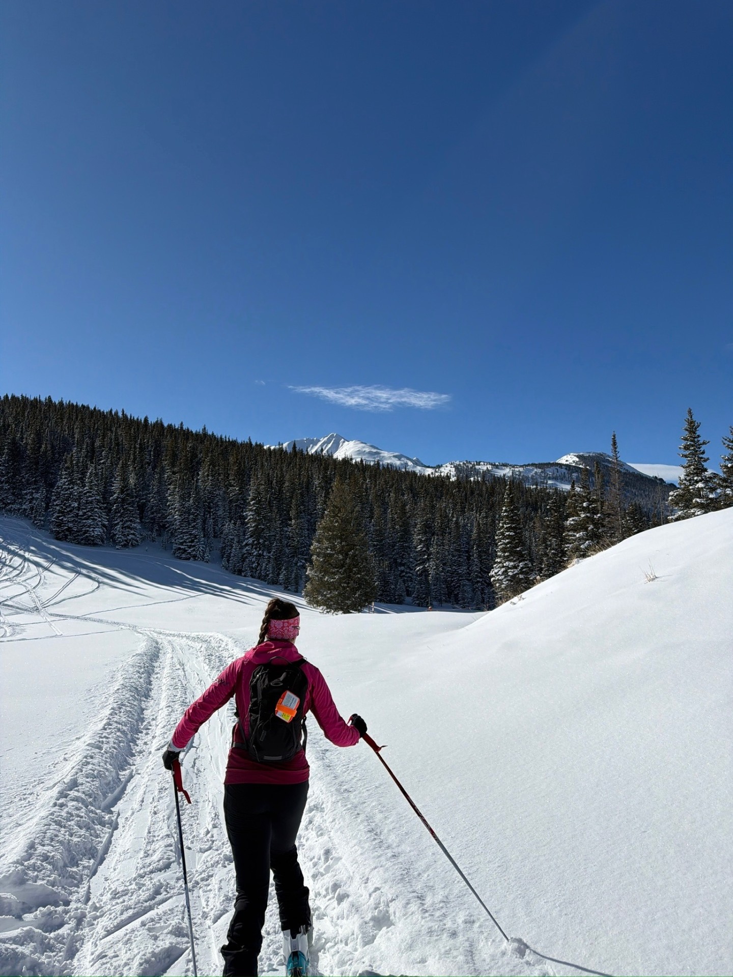 Bayli skinning up a snowy track toward alpine peaks in a pink Rapha jacket