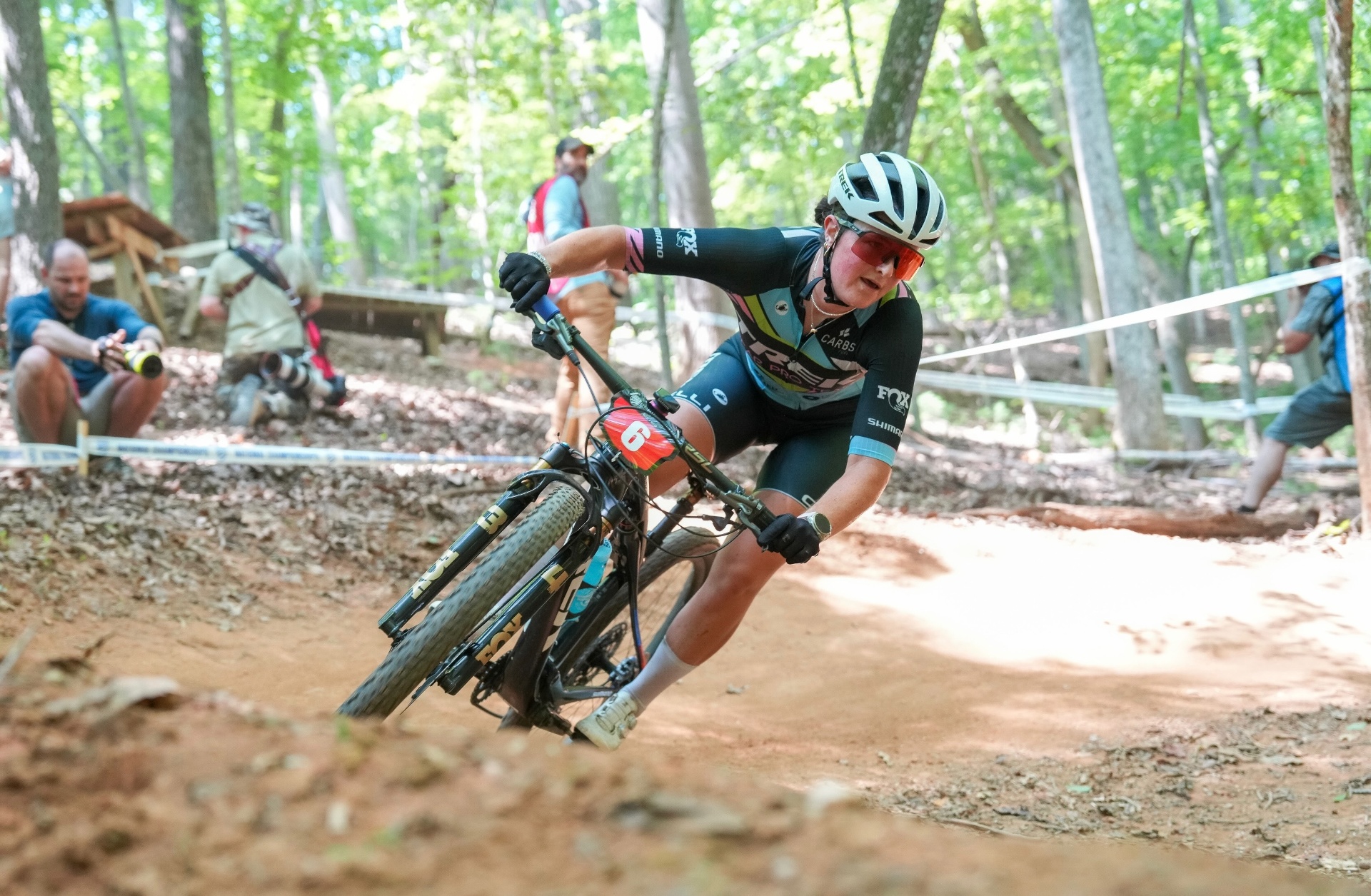 Bayli cornering hard in Trek Bear Pro kit through a wooded XCO course