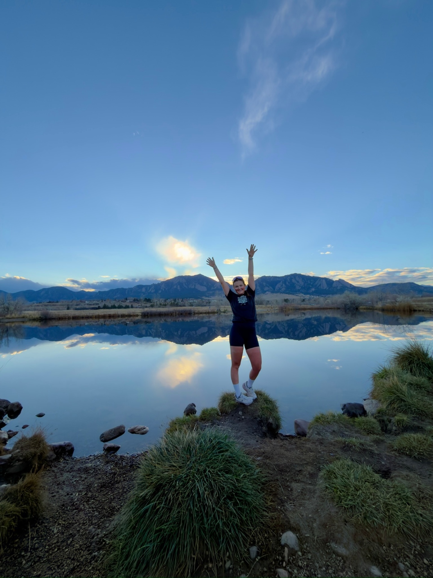 Bayli celebrating at sunrise in front of the Boulder Flatirons reflected in a still pond