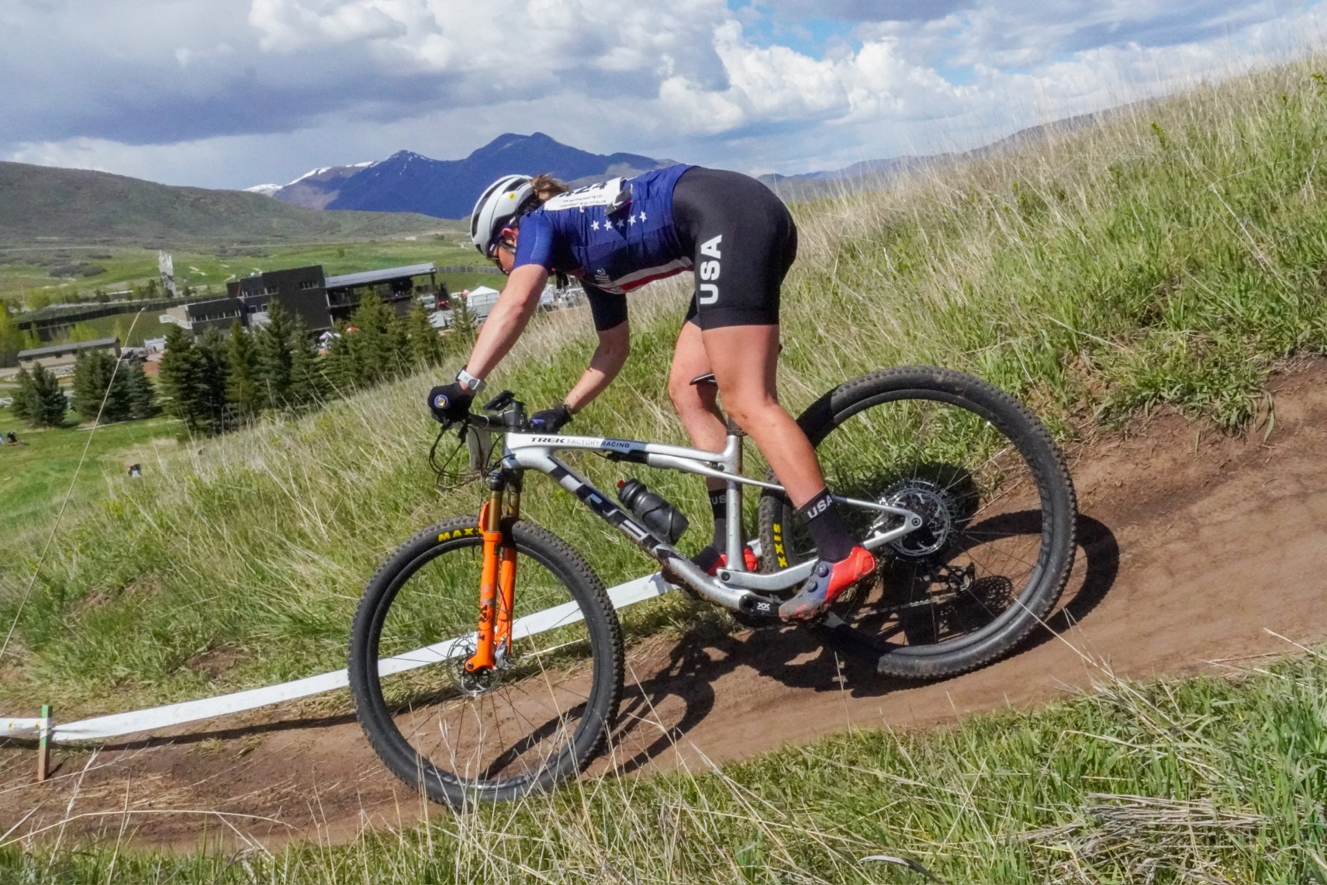 Bayli in USA kit descending a berm at Soldier Hollow with mountains behind