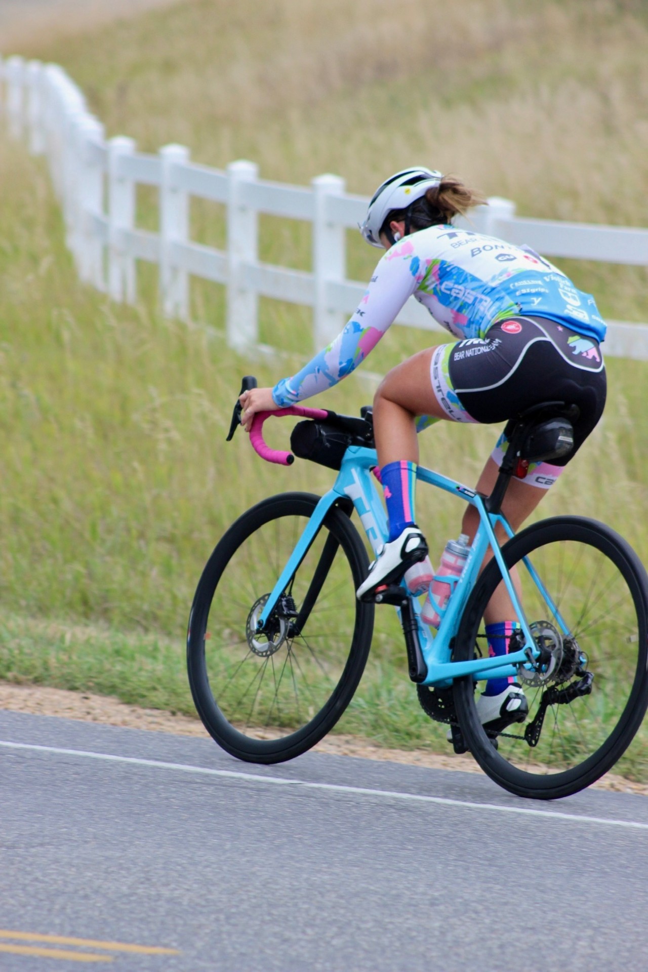 Bayli riding away on a Trek road bike with pink bar tape along a white fence